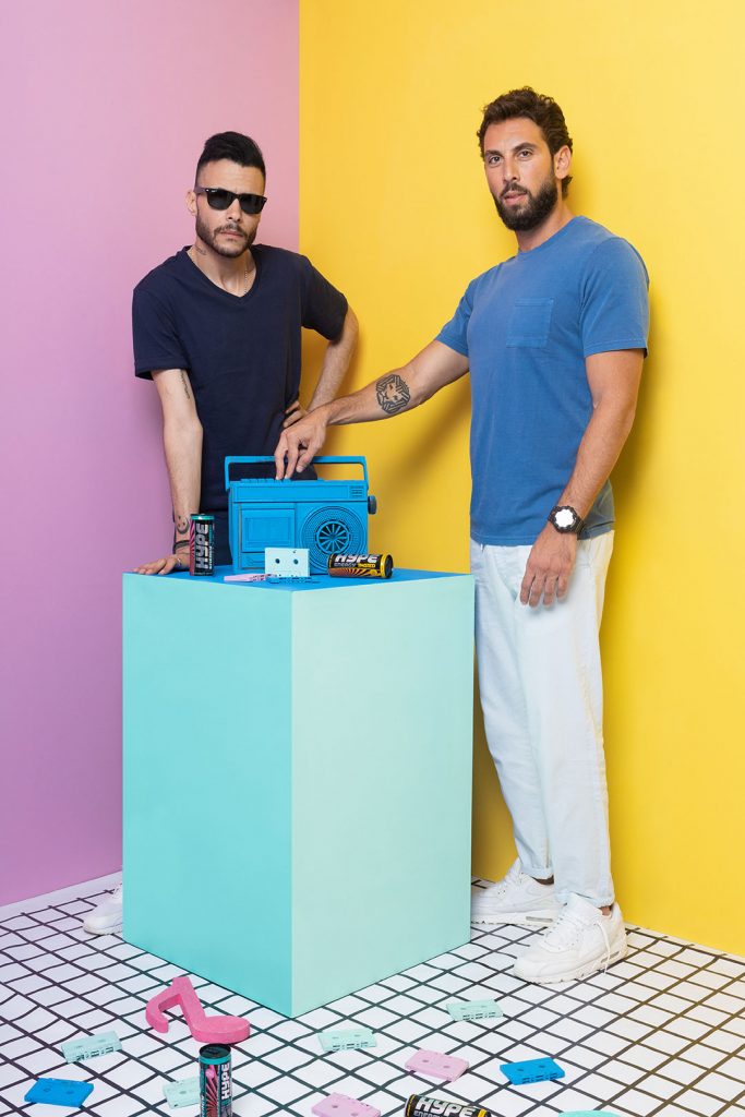 Two guy posing in front of the wall.